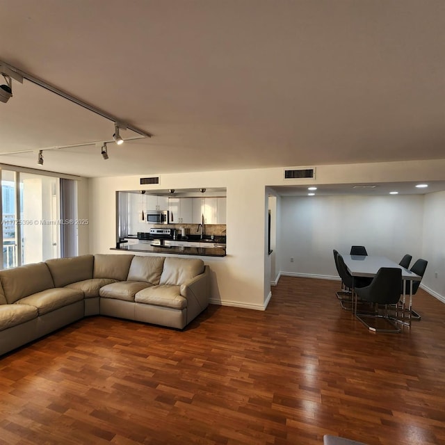 living room with sink, track lighting, and dark wood-type flooring