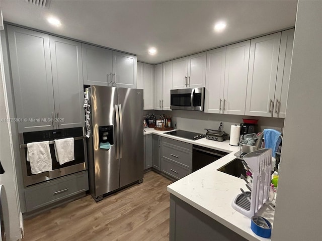 kitchen with light stone countertops, appliances with stainless steel finishes, gray cabinets, and light hardwood / wood-style flooring