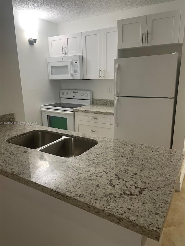 kitchen featuring white appliances, kitchen peninsula, a textured ceiling, and white cabinetry