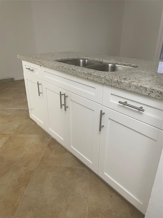 room details featuring white cabinets, light stone counters, and sink