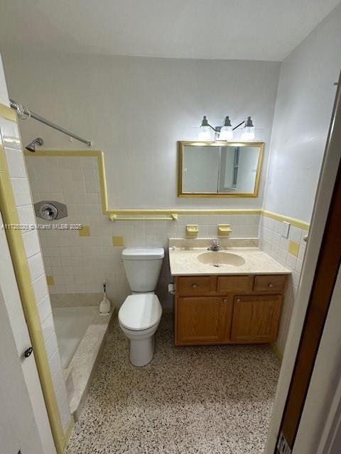 bathroom with tile walls, tiled shower, vanity, and toilet