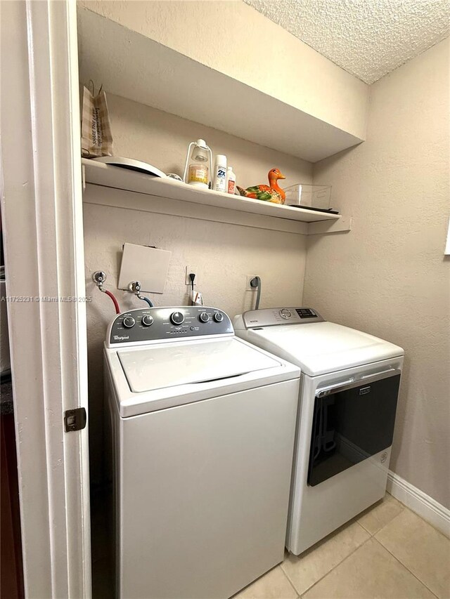 clothes washing area with light tile patterned flooring, a textured ceiling, and separate washer and dryer