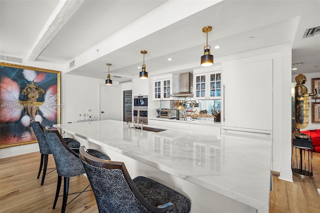 kitchen with light stone countertops, pendant lighting, white cabinets, wall chimney exhaust hood, and decorative backsplash