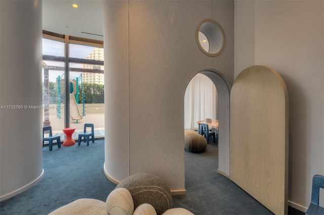 hallway featuring expansive windows and dark colored carpet