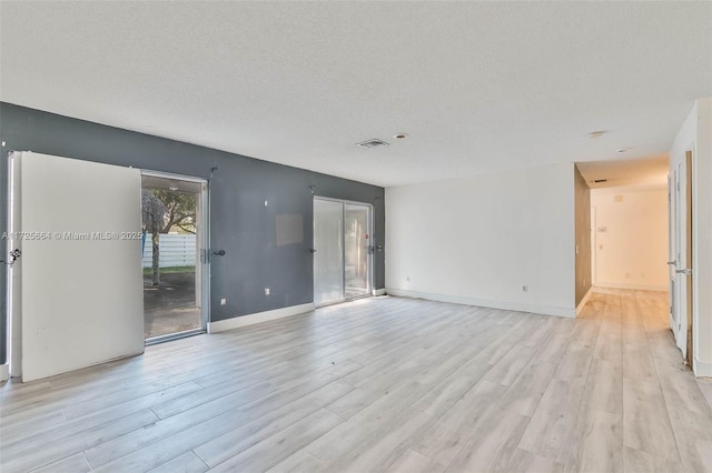 spare room with baseboards, visible vents, a textured ceiling, and light wood finished floors