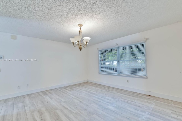 empty room featuring wood finished floors, a textured ceiling, baseboards, and an inviting chandelier