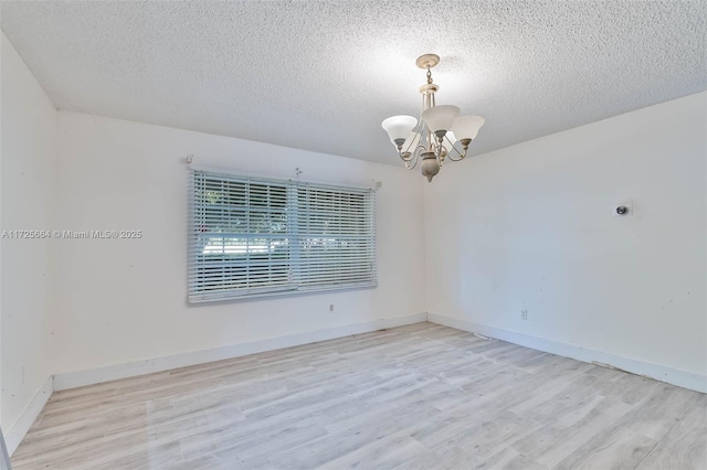 spare room with an inviting chandelier, baseboards, light wood finished floors, and a textured ceiling