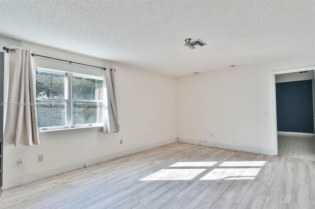 spare room featuring baseboards, light wood-style flooring, visible vents, and a textured ceiling