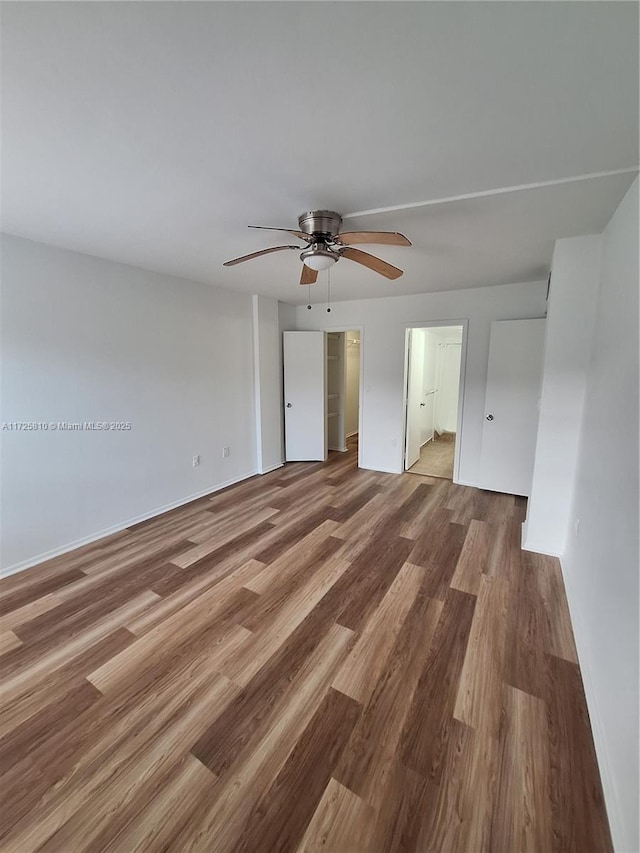 unfurnished bedroom with ensuite bathroom, wood finished floors, a ceiling fan, and baseboards