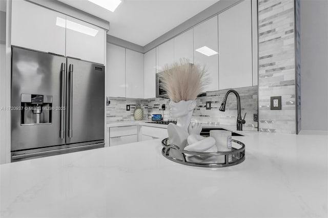 kitchen featuring stainless steel fridge with ice dispenser, light stone counters, decorative backsplash, sink, and white cabinetry