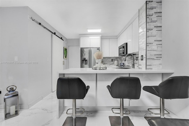 kitchen with stainless steel appliances, white cabinets, a kitchen breakfast bar, kitchen peninsula, and a barn door