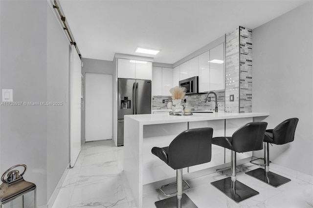 kitchen featuring stainless steel appliances, sink, white cabinetry, a kitchen breakfast bar, and kitchen peninsula