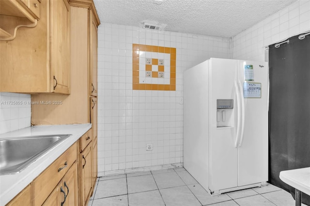 kitchen featuring light brown cabinetry, a textured ceiling, tile walls, light tile patterned floors, and white refrigerator with ice dispenser