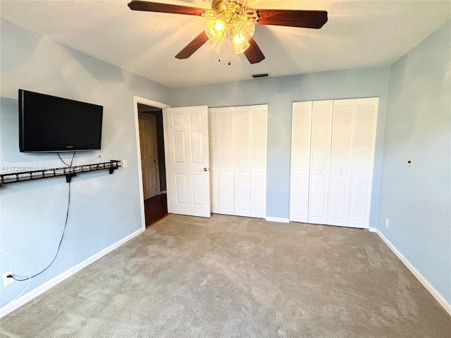 unfurnished bedroom featuring two closets, ceiling fan, and light carpet