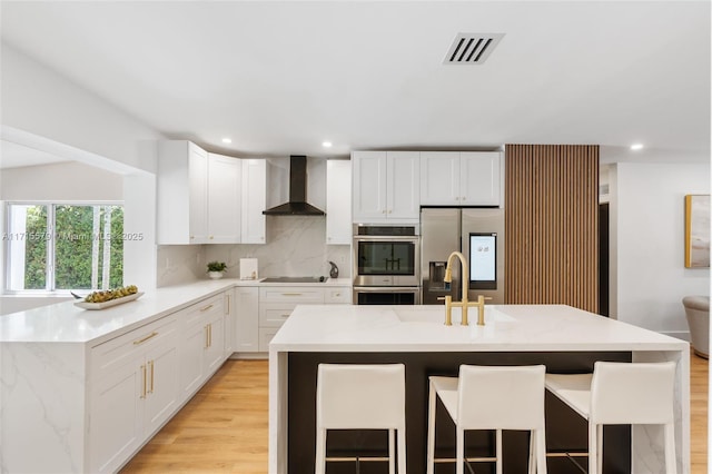 kitchen featuring appliances with stainless steel finishes, a kitchen bar, white cabinetry, wall chimney range hood, and tasteful backsplash