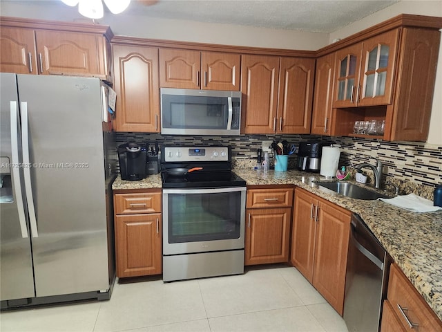 kitchen featuring appliances with stainless steel finishes, light stone countertops, light tile patterned floors, sink, and backsplash