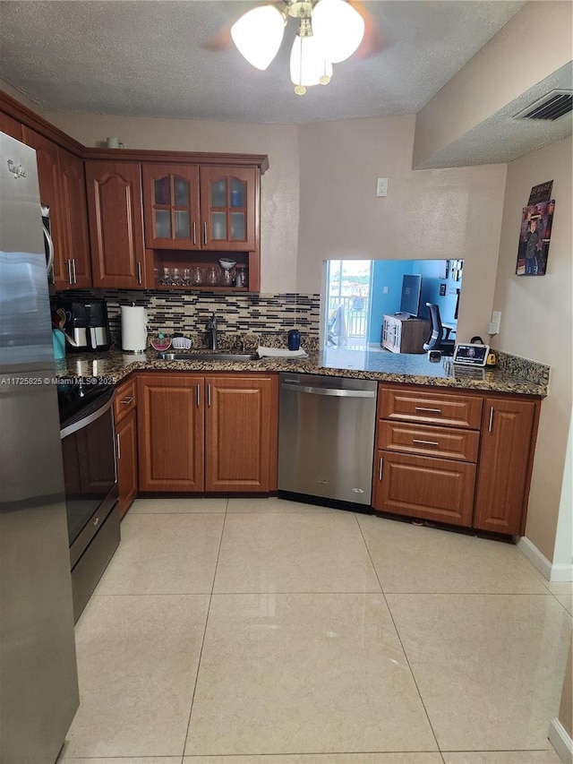 kitchen with appliances with stainless steel finishes, dark stone countertops, light tile patterned floors, and sink