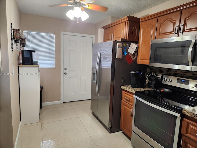 kitchen with appliances with stainless steel finishes, ceiling fan, light stone counters, and light tile patterned floors