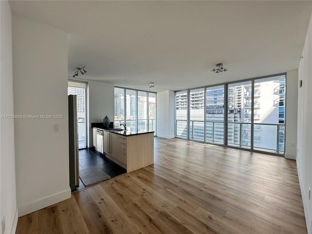 interior space featuring floor to ceiling windows, a sink, open floor plan, dark countertops, and wood finished floors