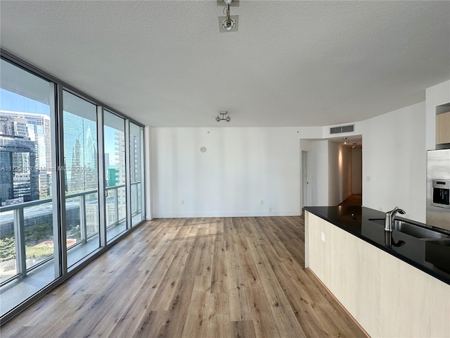 unfurnished living room with light wood-type flooring, a textured ceiling, visible vents, a wall of windows, and a sink