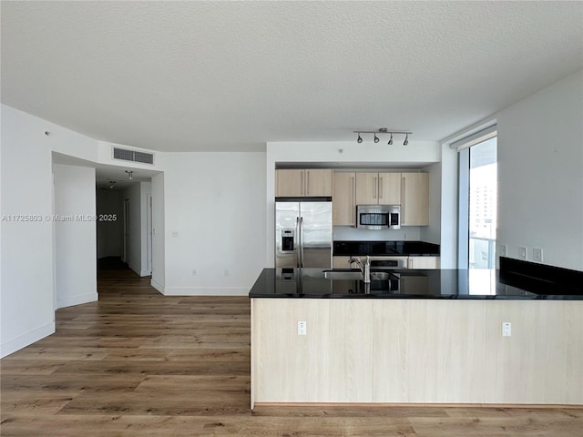 kitchen with light brown cabinets, dark countertops, visible vents, stainless steel appliances, and wood finished floors