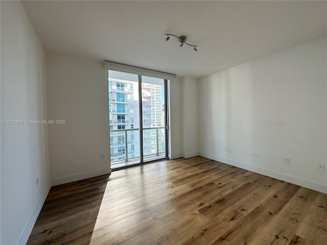 spare room featuring wood finished floors, floor to ceiling windows, and baseboards