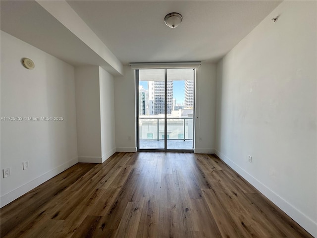 unfurnished room featuring baseboards, a view of city, wood finished floors, and expansive windows