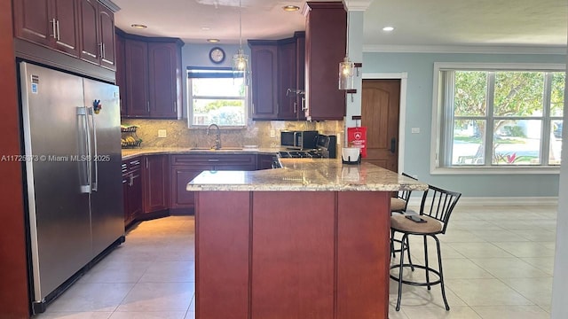 kitchen featuring sink, a kitchen breakfast bar, ornamental molding, light tile patterned floors, and stainless steel fridge