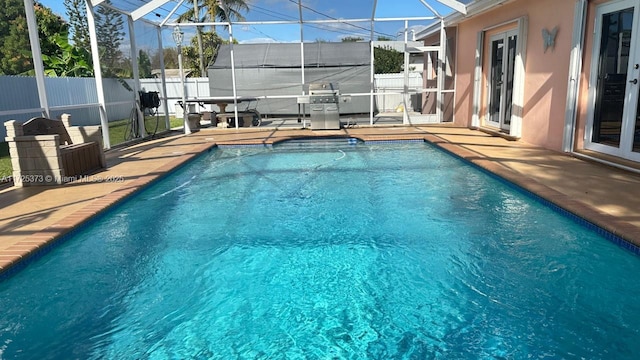 view of pool featuring glass enclosure, grilling area, and a patio