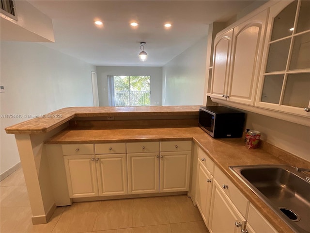 kitchen with kitchen peninsula, decorative light fixtures, white cabinets, light tile patterned flooring, and sink