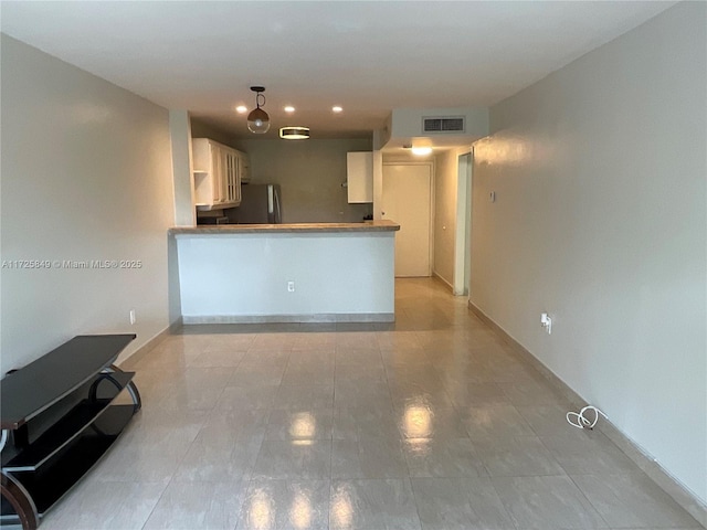 kitchen featuring kitchen peninsula, light tile patterned flooring, stainless steel fridge, and white cabinets