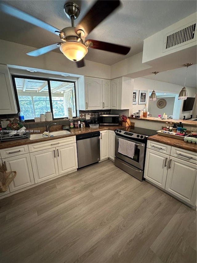 kitchen featuring light hardwood / wood-style flooring, decorative light fixtures, white cabinetry, appliances with stainless steel finishes, and sink