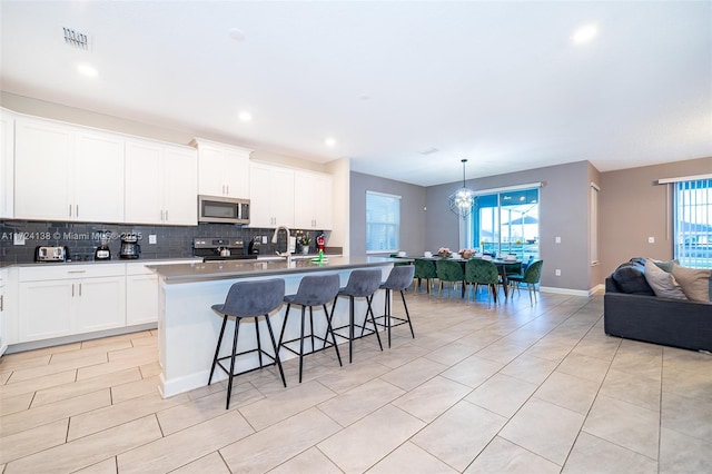 kitchen with an island with sink, a kitchen bar, an inviting chandelier, white cabinetry, and appliances with stainless steel finishes