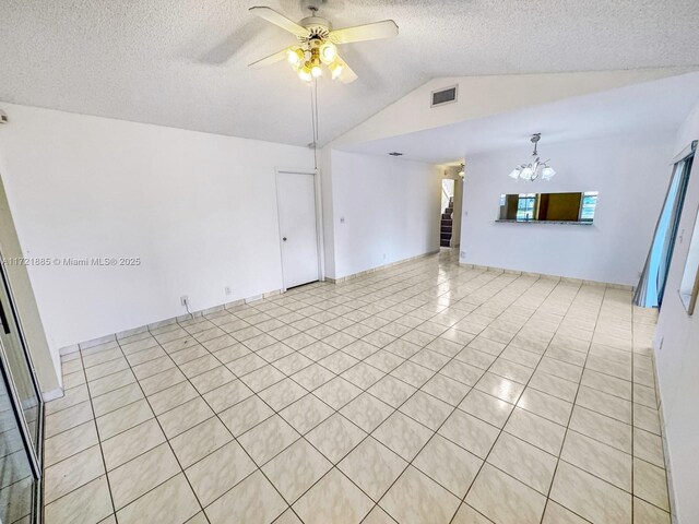 empty room featuring ceiling fan with notable chandelier, a textured ceiling, light tile patterned flooring, and vaulted ceiling