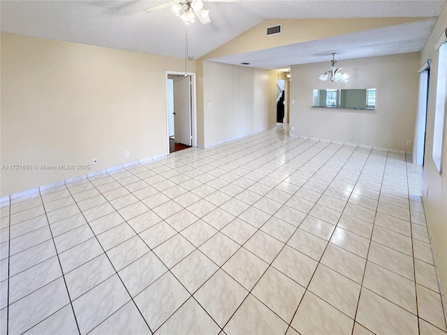 unfurnished room featuring ceiling fan with notable chandelier, light tile patterned flooring, a textured ceiling, and vaulted ceiling