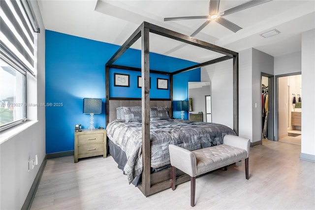 bedroom with ceiling fan, light wood-style flooring, a closet, a walk in closet, and baseboards