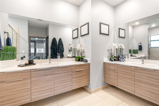 full bath featuring two vanities, baseboards, a stall shower, tile patterned flooring, and a sink