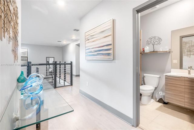hall featuring a sink, visible vents, baseboards, and an upstairs landing