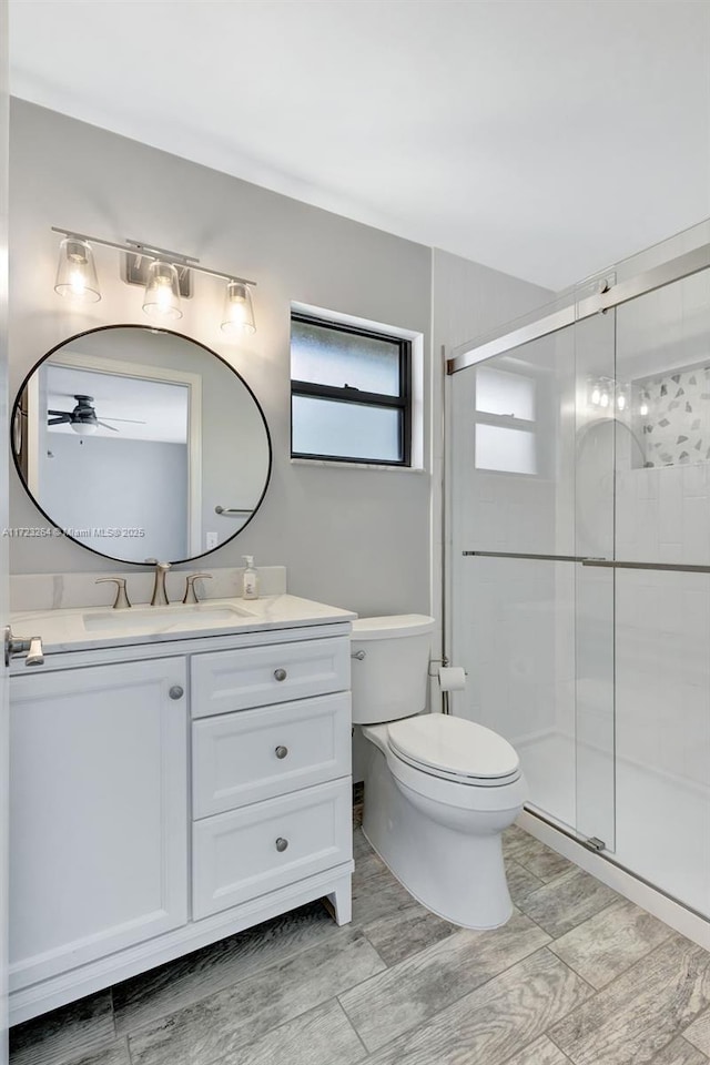 bathroom with toilet, a shower with door, ceiling fan, and vanity