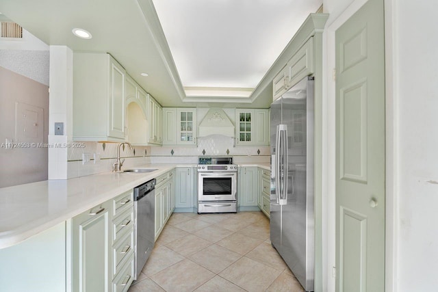 kitchen with sink, a raised ceiling, light tile patterned floors, kitchen peninsula, and appliances with stainless steel finishes