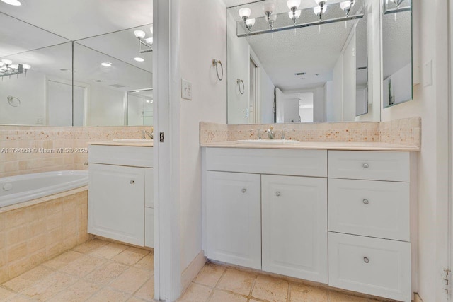 bathroom with tile patterned flooring, a relaxing tiled tub, backsplash, and vanity