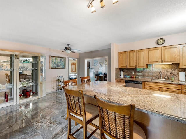 kitchen with light stone countertops, ceiling fan, tasteful backsplash, and sink