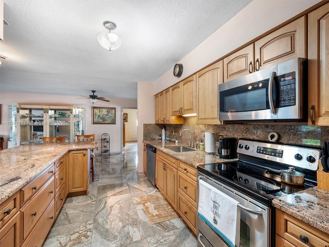 kitchen featuring ceiling fan, backsplash, sink, appliances with stainless steel finishes, and light stone countertops