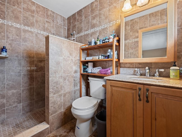 bathroom with tile walls, tiled shower, vanity, and toilet