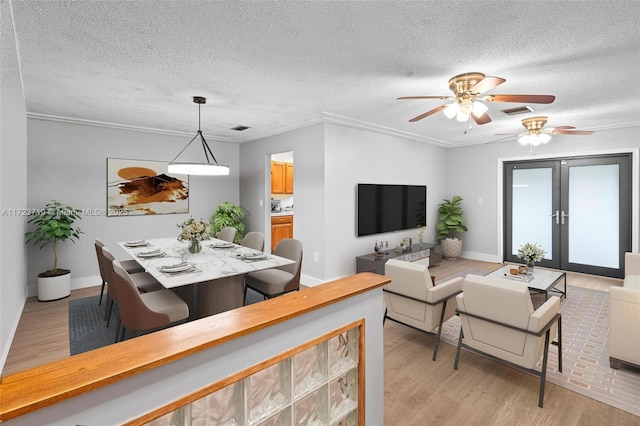 dining area featuring light wood-type flooring, french doors, ornamental molding, and a textured ceiling