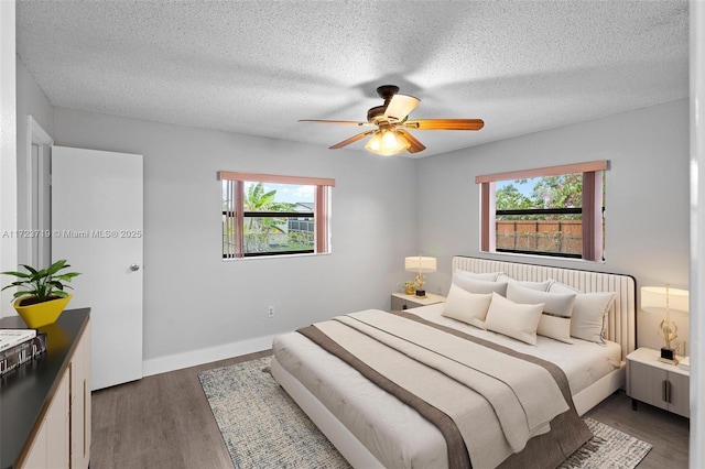 bedroom with ceiling fan, dark wood-type flooring, multiple windows, and a textured ceiling