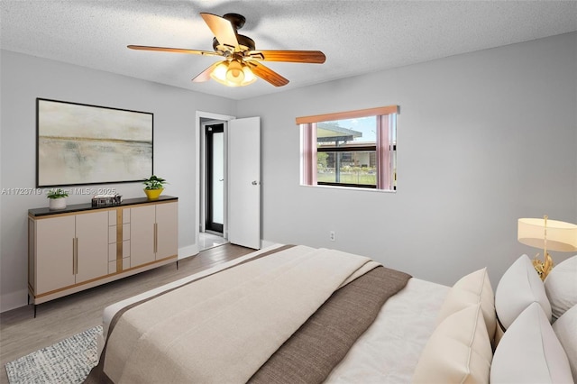 bedroom with ceiling fan, light wood-type flooring, and a textured ceiling