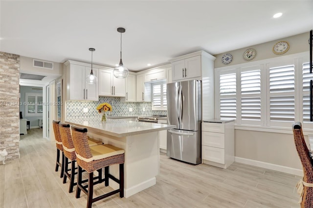 kitchen with decorative light fixtures, tasteful backsplash, white cabinetry, stainless steel refrigerator, and a kitchen breakfast bar