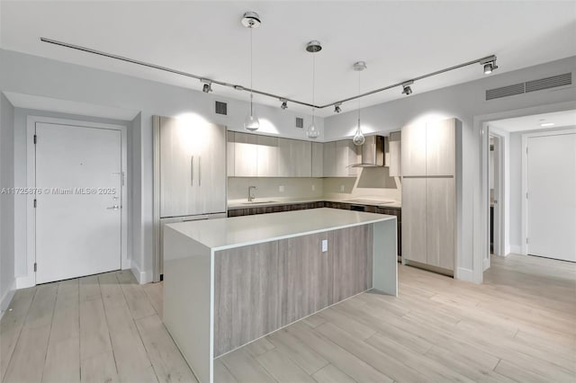 kitchen with sink, wall chimney exhaust hood, hanging light fixtures, a kitchen island, and stovetop