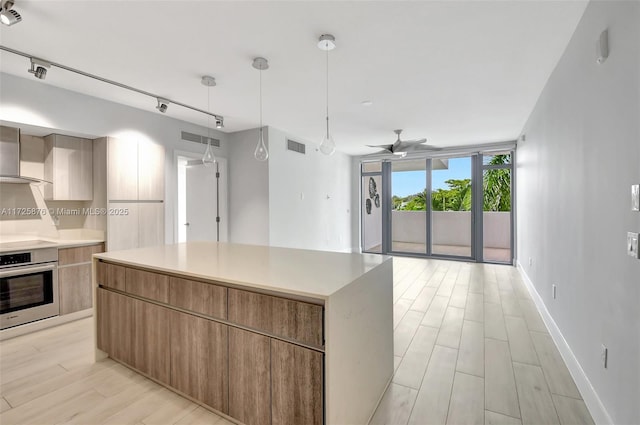 kitchen with hanging light fixtures, a center island, stainless steel oven, ceiling fan, and wall chimney exhaust hood